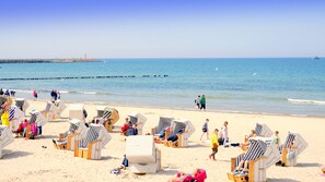 A beach with rows of striped beach chairs and umbrellas, a sandy shore, and a calm sea. - Family-friendly apartment, playground, parking. (Kołobrzeg)