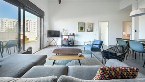 Una sala moderna con un sofá, una mesa de centro y un televisor. Hay un comedor con sillas y una mesa.