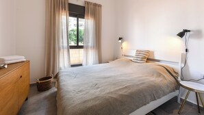 Un dormitorio con cama, lámpara de noche, mesita de noche, cómoda y ventana con cortinas.