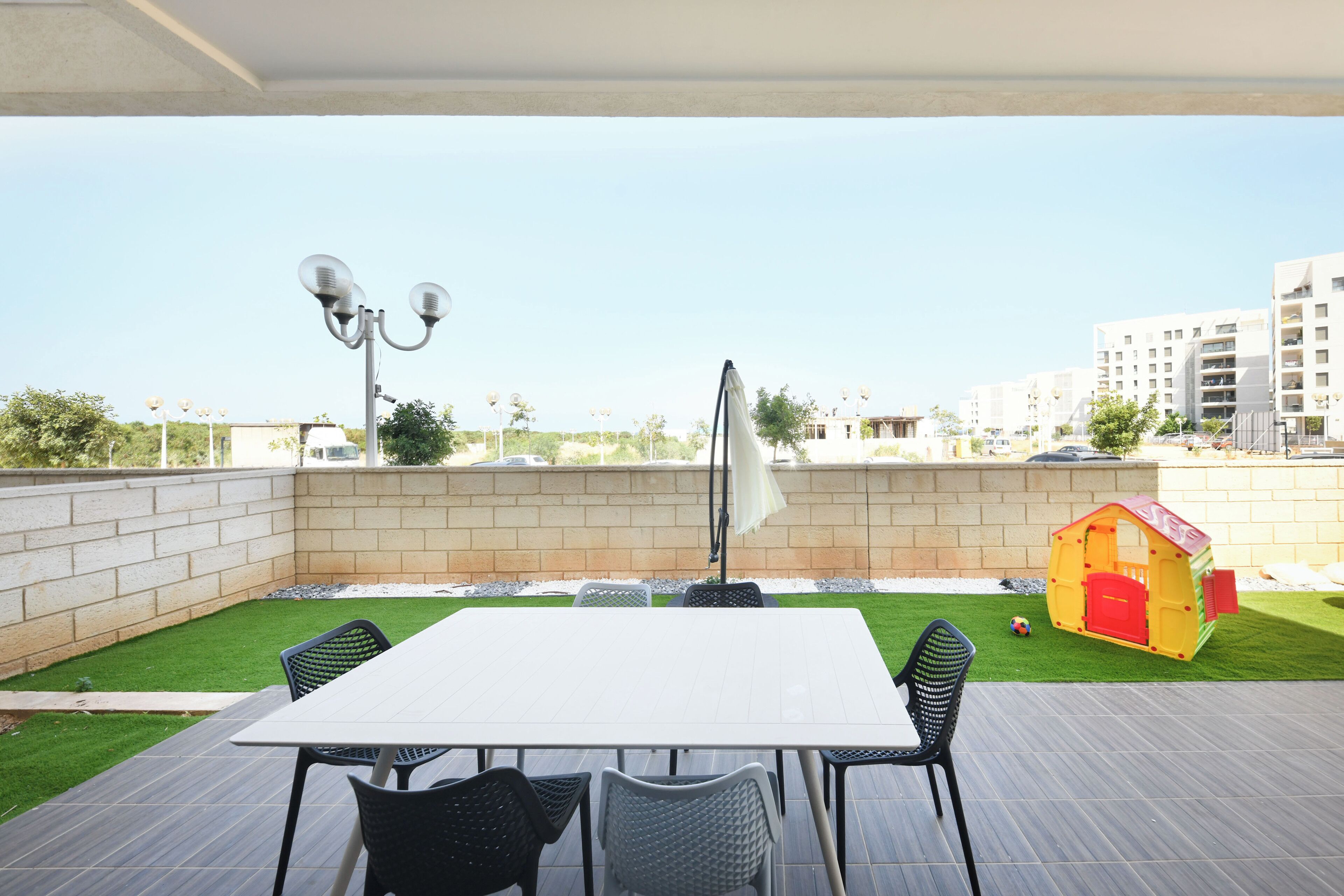 Een terras buiten met een tafel, stoelen, een speeltuintje en gebouwen in de verte.