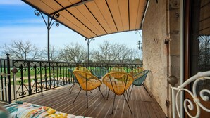 Ein Balkon mit Holzboden, gelben und grünen Stühlen und einem beige farbenen Baldachin.