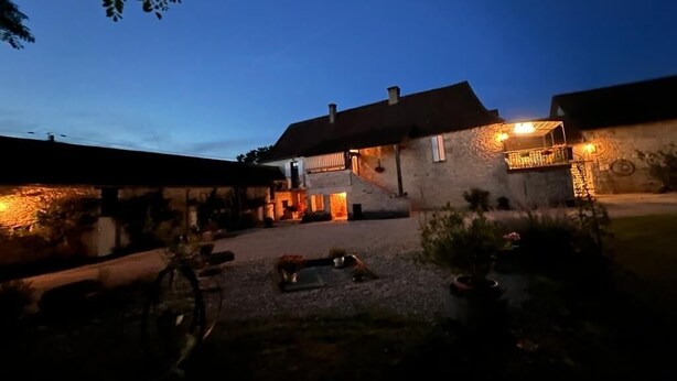 Ein Gebäude aus Stein mit einer überdachten Terrasse, Sitzgelegenheiten im Freien und einem Kieshof.