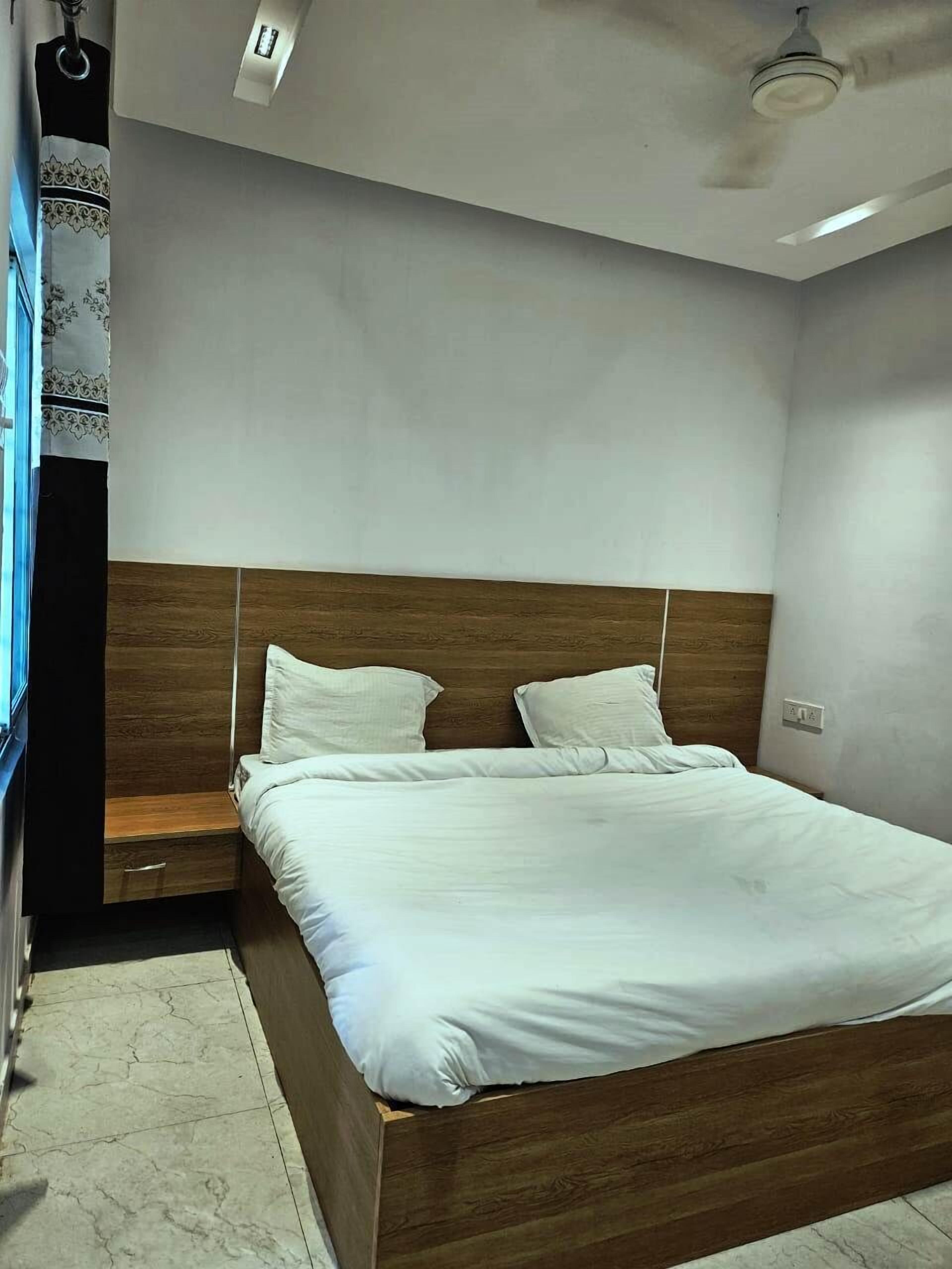 A modern bedroom with a wooden headboard, a single bed with white bedding, a nightstand, and a small drawer.