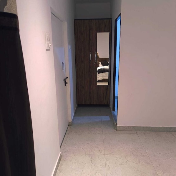 A narrow hallway with a wooden door and a mirror reflecting a bed.