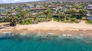 An aerial view of a coastal resort with beachfront properties, clear turquoise waters, and a backdrop of mountains.