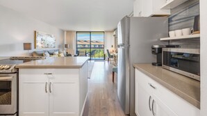 A modern kitchen with white cabinets, a large island, and a view to a balcony.