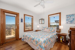 Un dormitorio con una cama grande, dos ventanas, un ventilador de techo y vistas al exterior.