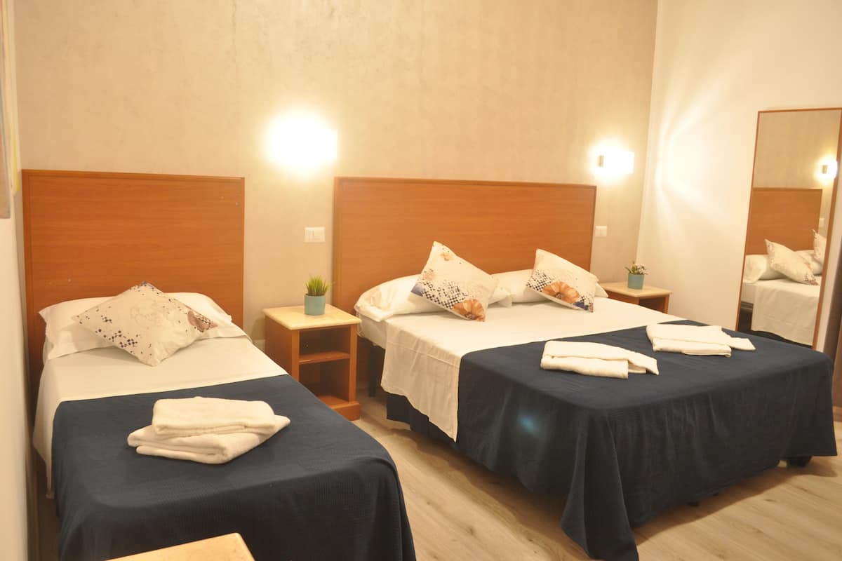 Ein Hotelzimmer mit zwei Einzelbetten, jeweils mit einem hölzernen Kopfteil, weißer Bettwäsche und einem kleinen Nachttisch mit einer Pflanze.