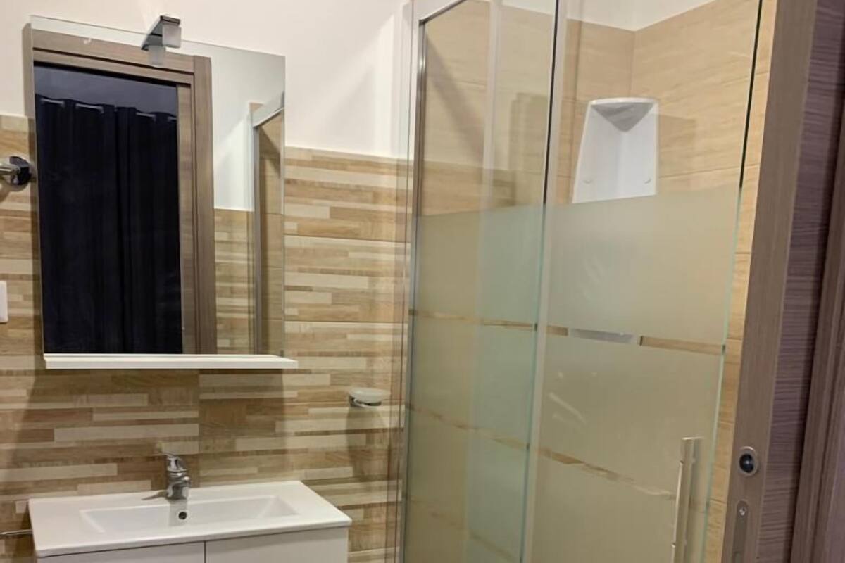 Ein modernes Badezimmer mit Duschkabine aus Glas, einem weißen Waschbecken und einem Spiegel darüber.