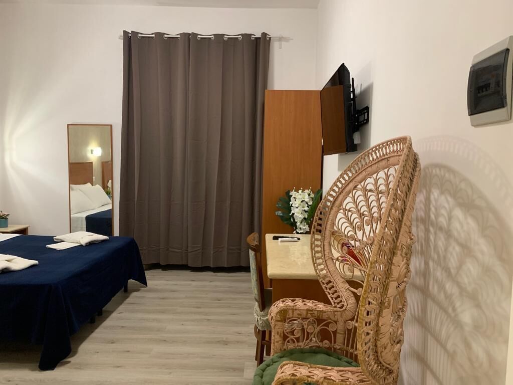 A hotel room with a bed, a chair, a desk, a mirror, and a curtain.