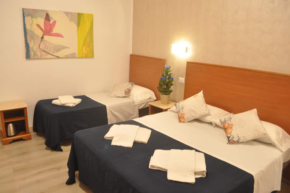 Ein Hotelzimmer mit zwei Einzelbetten, einem Nachttisch mit Lampe, einem kleinen Holztischchen und einem Wandbild.