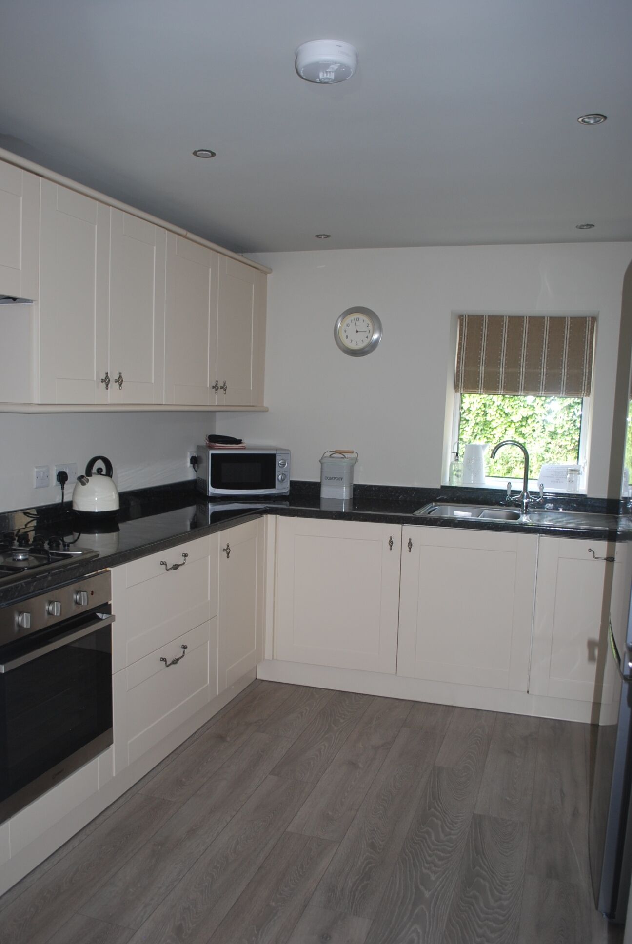 A modern kitchen with white cabinets, a microwave, a kettle, and a sink.