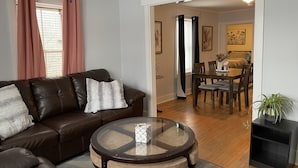 Un salon avec un canapé en cuir marron, une table basse en verre et un coin repas doté de meubles en bois.