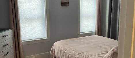 Un dormitorio con cama, cómoda y dos ventanas con cortinas.