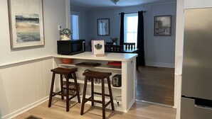 Une cuisine avec un îlot central blanc, des tabourets en bois, un four à micro-ondes, un grille-pain et un réfrigérateur.