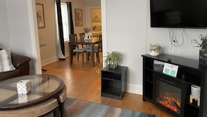 Un salon doté d’une cheminée, d’un téléviseur fixé au mur et d’un coin repas avec une table et des chaises.