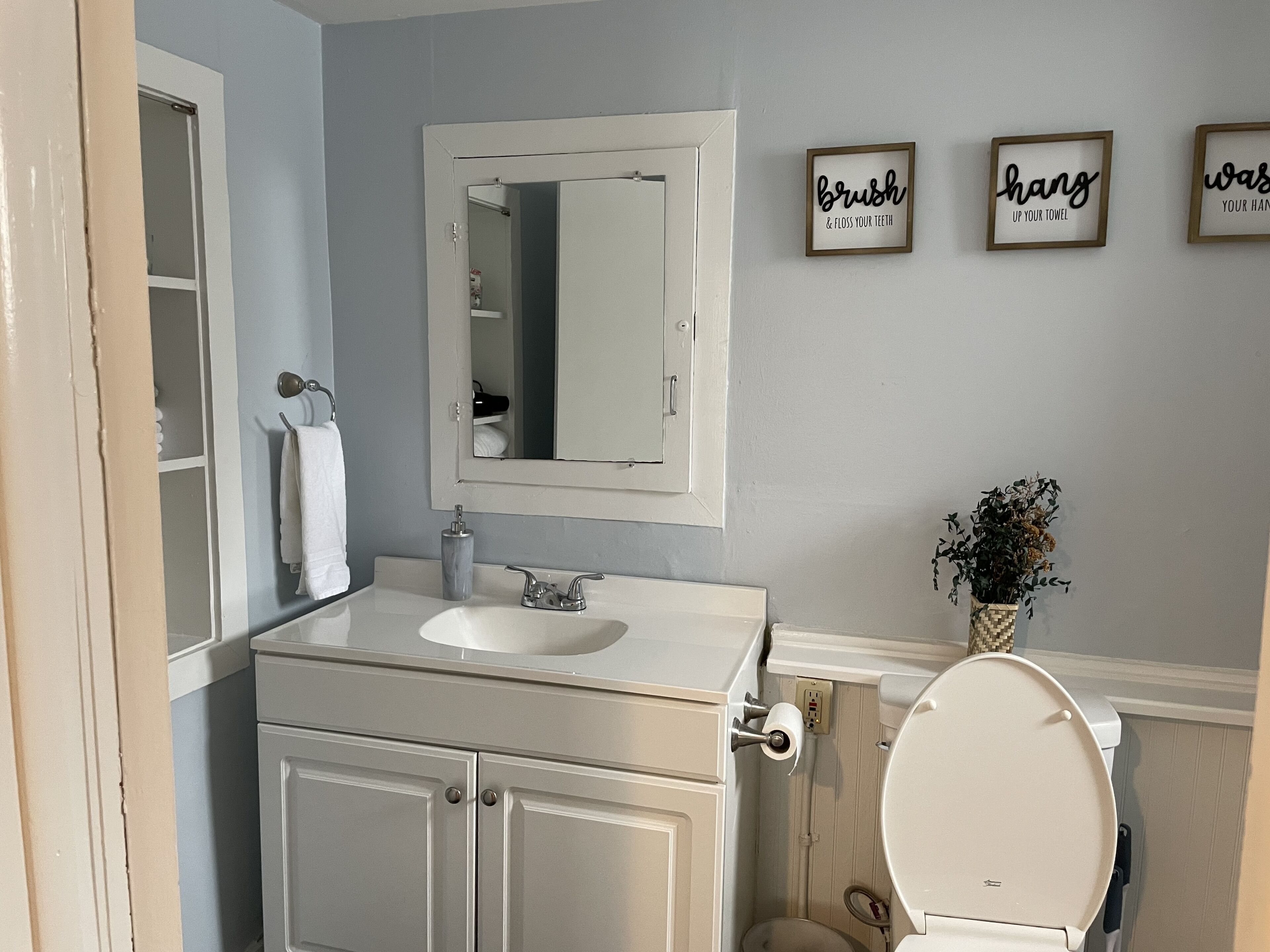 Ein Badezimmer mit einem weißen Waschbecken, einem Spiegel, einer Toilette und drei gerahmten Schildern an der Wand.