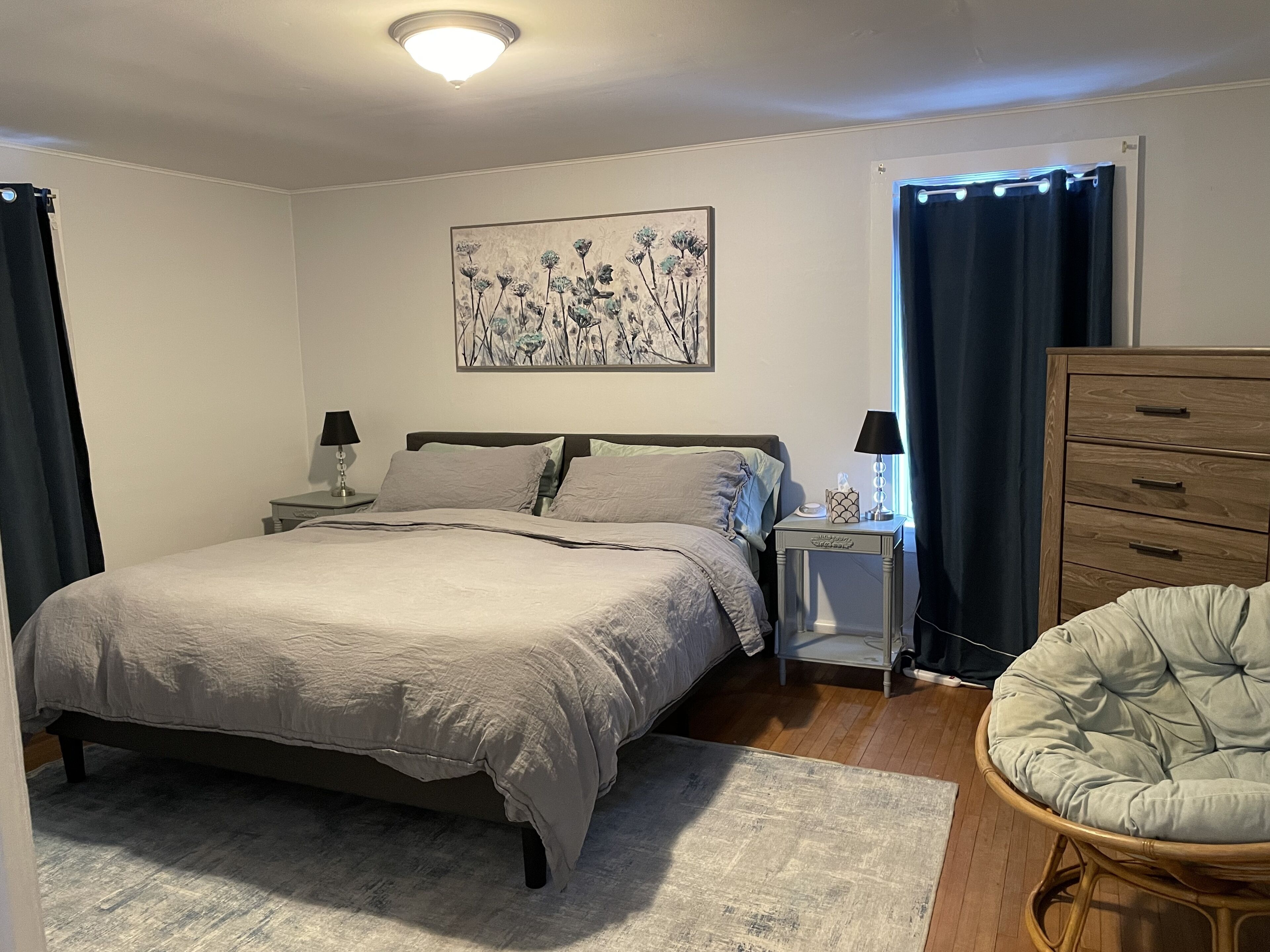 A bedroom with a bed, bedside tables, a dresser, a chair, and a painting on the wall.