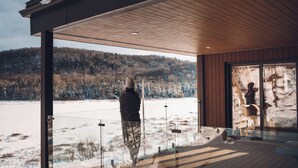 Ein modernes Gebäude mit einer Holzterrasse und großen Fenstern mit Blick auf eine verschneite Landschaft.