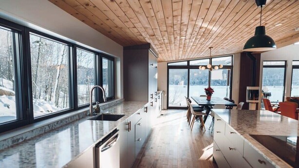 Eine moderne Küche mit großen Fenstern, Holzboden und einem Essbereich mit Blick ins Freie.