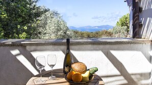 Una mesa con una botella, vasos y fruta en un balcón con vistas al paisaje.