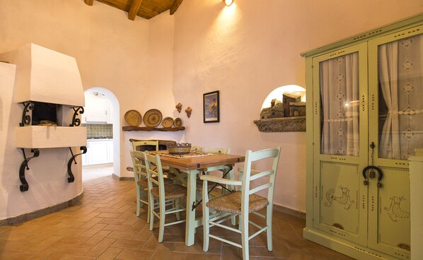 Un coin repas avec une table en bois et quatre chaises, un meuble orné de motifs décoratifs, et une petite cuisine équipée d’une cuisinière blanche.