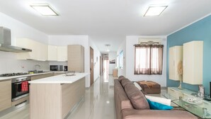 A modern kitchen with a central island, a dining area with a glass table, and a living space with a sofa and a TV. - ☆Amazing Apart.w/side Sea View☆8 (San Pawl il-Bahar)