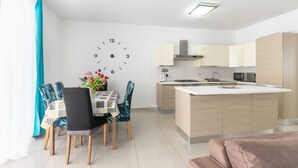 A modern kitchen with a central island, a dining area with a clock on the wall, and a living area with a sofa. - ☆Amazing Apart.w/side Sea View☆8 (San Pawl il-Bahar)