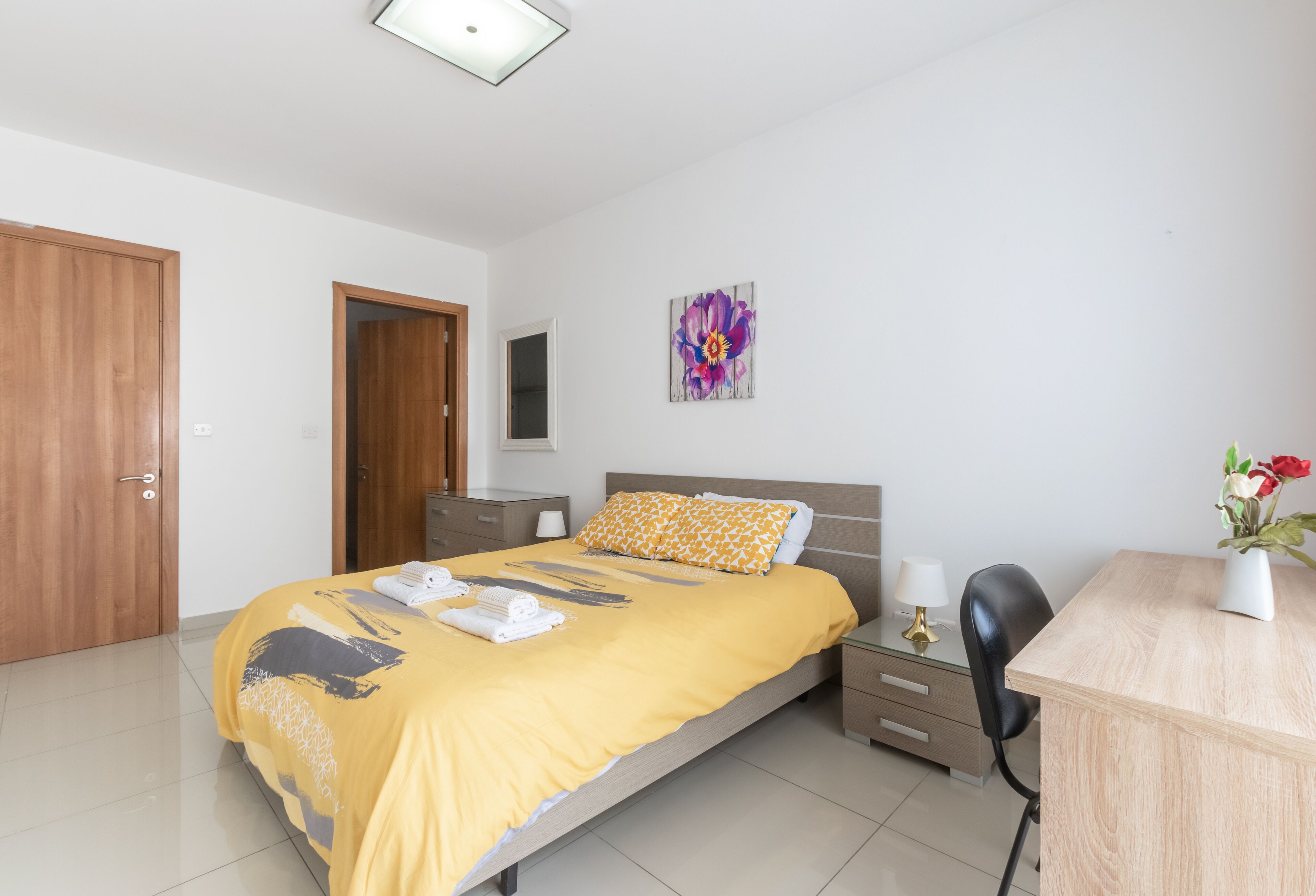 Une chambre d’hôtel comprenant un lit, un bureau, une chaise, une table de chevet, une armoire et un tableau au mur.