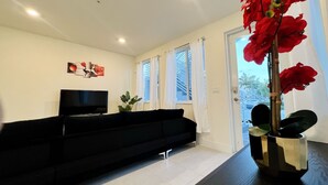 Ein modernes Wohnzimmer mit einer schwarzen Couch, einem Flachbildfernseher und einer Topfpflanze.