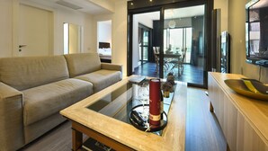 A modern living room with a sofa, a glass coffee table, and a TV on a wooden cabinet. - Luxury Levontin apt near Rothschild (Tel Aviv)