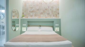 A neatly made bed with a beige blanket, a large mirror, and a patterned wall above it.