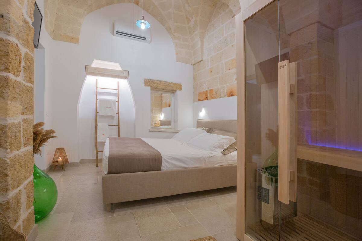 A bedroom with a bed, a mirror, a ladder, and a glass door leading to a bathroom.
