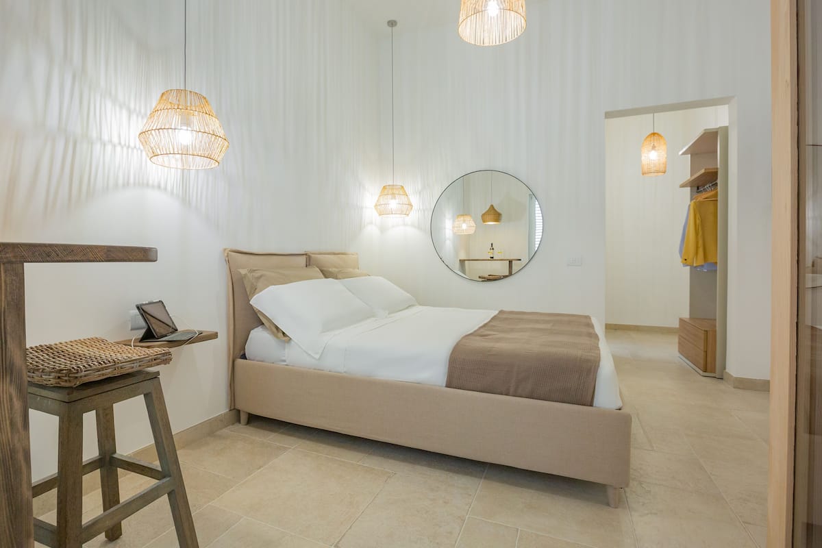 A bedroom with a bed, bedside table, lamp, mirror, and a wardrobe.