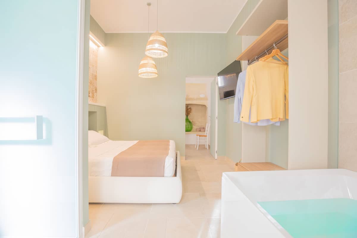 A modern hotel room with a bed, a small seating area, and a wardrobe with hanging clothes.