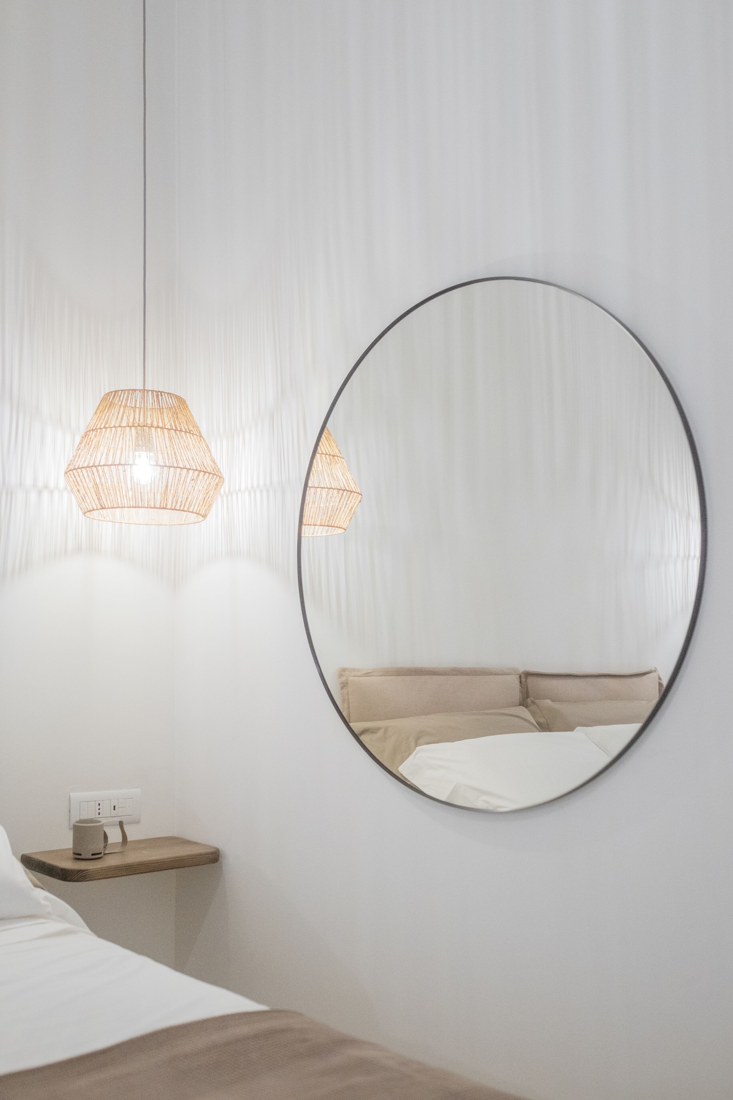 A minimalist bedroom with a bed, bedside table, and a round mirror on the wall.