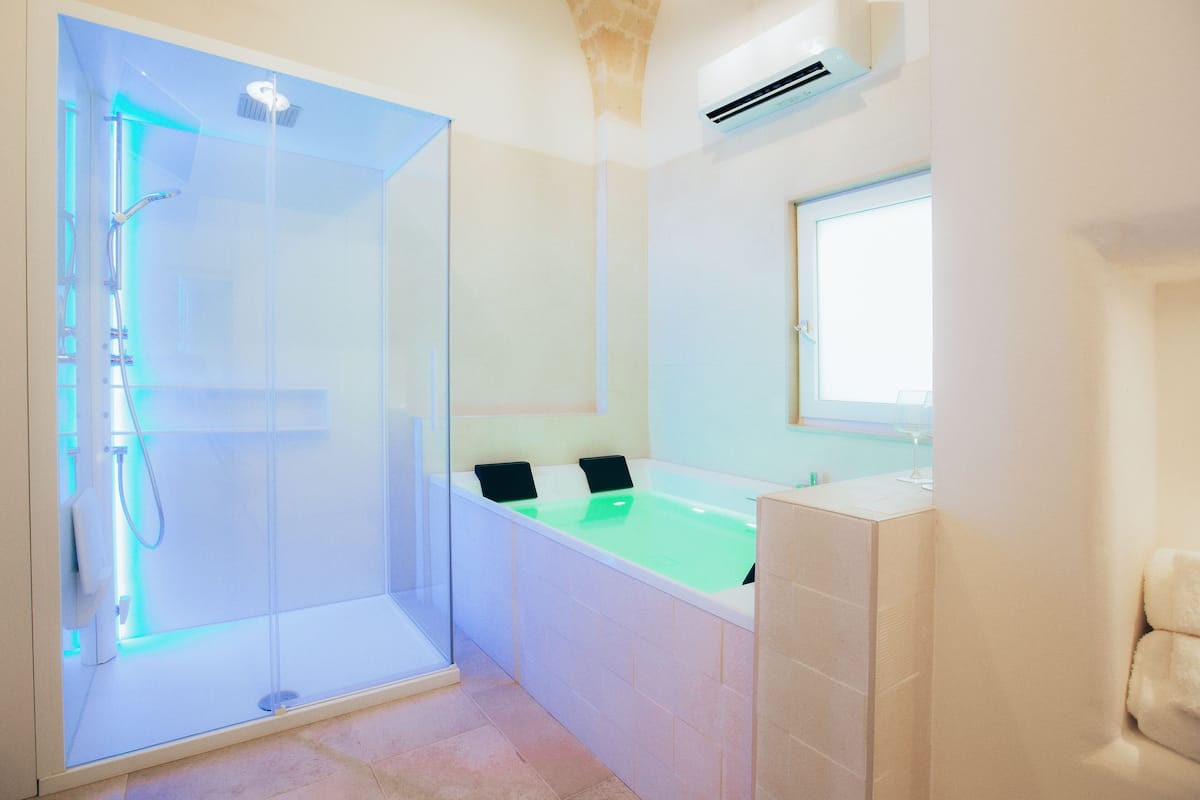 A modern bathroom with a glass-enclosed shower, a bathtub with green water, and a large mirror.