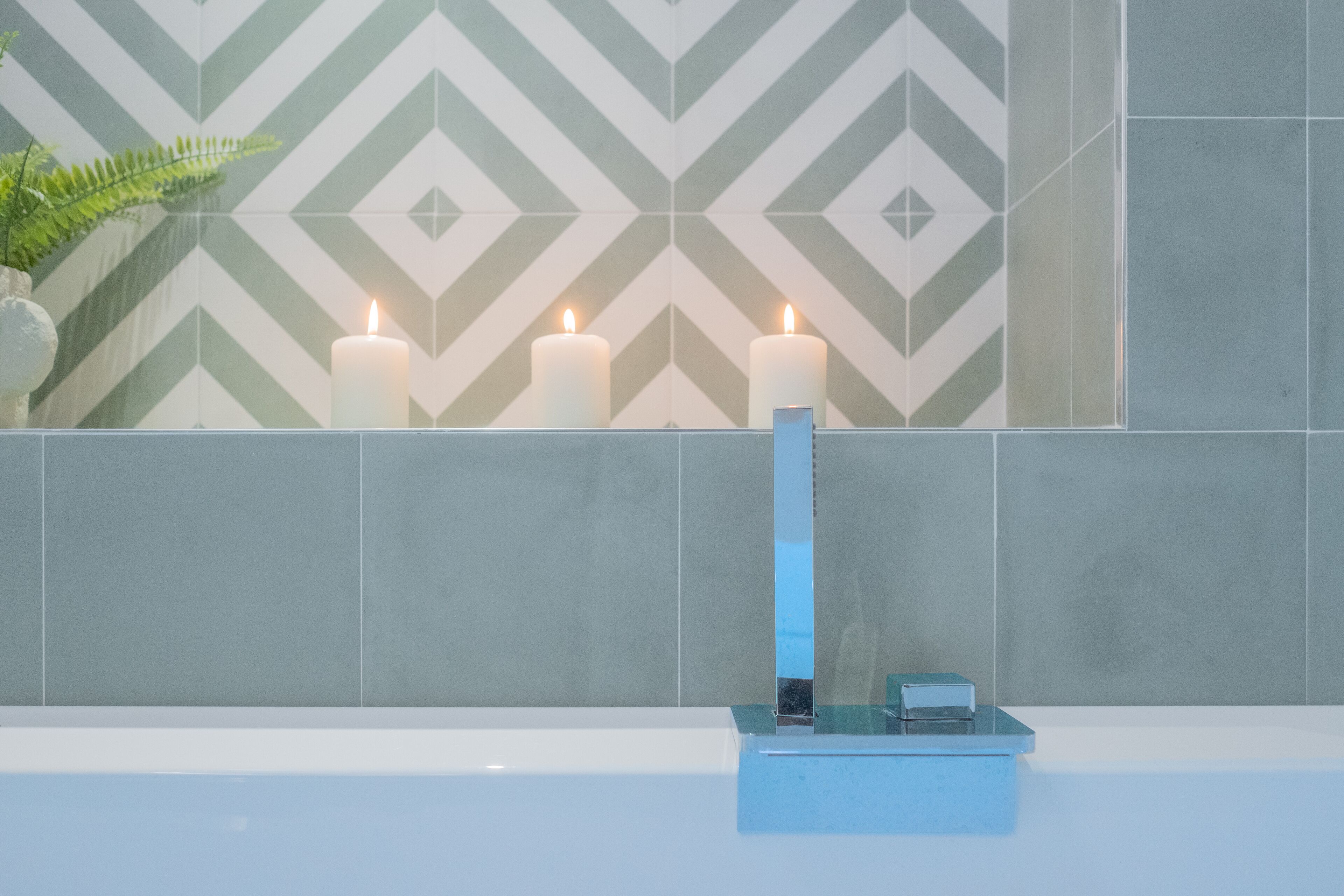 A bathroom with a geometric patterned wall, three lit candles, and a blue soap dish.