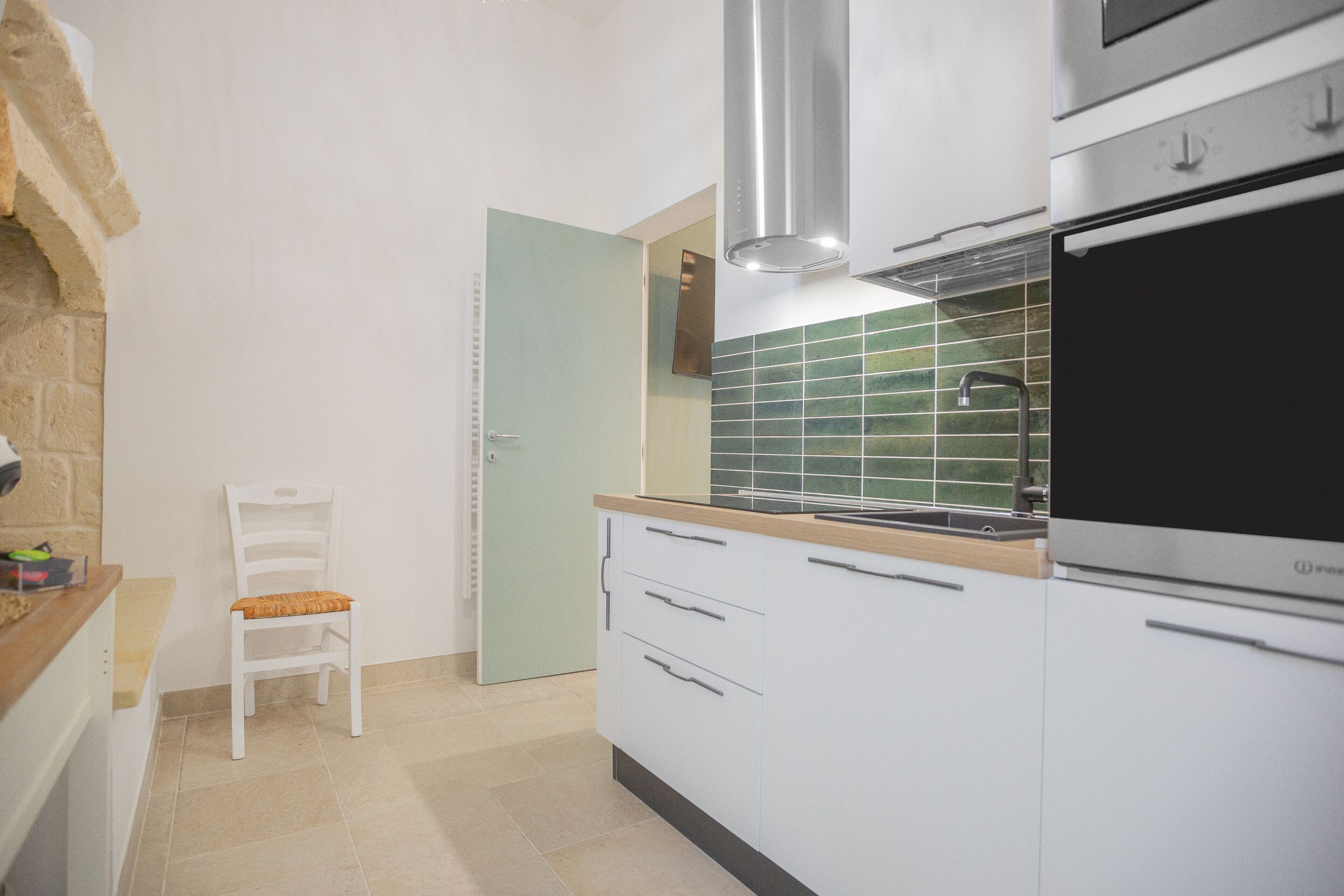A modern kitchen with white cabinets, a built-in oven, and a green-tiled backsplash.