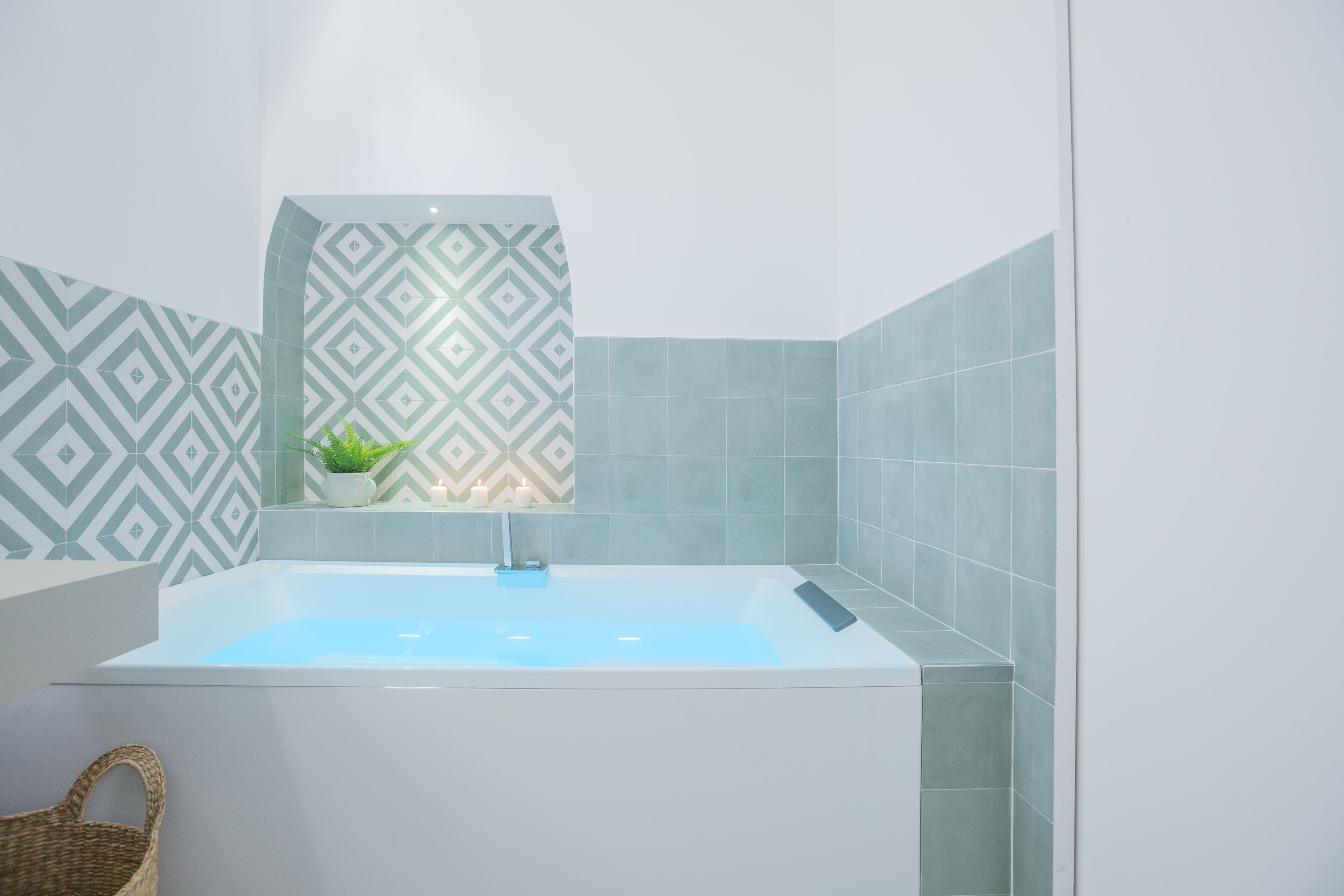 A modern bathroom with a freestanding bathtub, a small window with a plant, and patterned tiles.