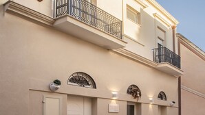En toetagers bygning med en flad facade, en indgang i stueetagen med en dør, og en lille balkon på øverste etage.