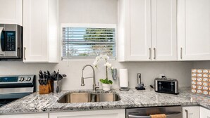 Eine moderne Küche mit weißen Schränken, einer Granit Arbeitsplatte, Edelstahlgeräten und einem Fenster mit Jalousien.