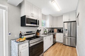 A modern kitchen with stainless steel appliances, white cabinetry, and a marble countertop.