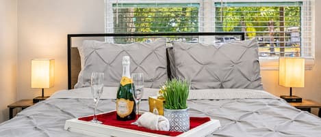A neatly made bed with a champagne bottle, glasses, and a tray.