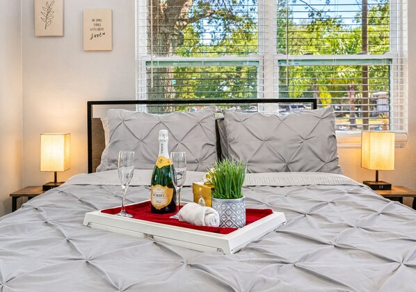 A neatly made bed with a champagne bottle, glasses, and a tray.