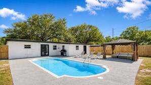 Ein Garten mit Swimmingpool, Grillplatz und überdachter Sitzgelegenheit.