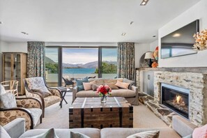 A living room with a sofa, chairs, a coffee table, a fireplace, and a large window with a view.