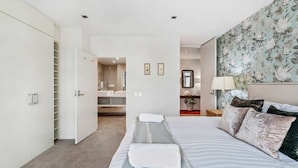 Un dormitorio con cama, armario, baño con espejo y pared con motivos florales.