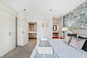A bedroom with a bed, a wardrobe, a bathroom with a mirror, and a floral wall.