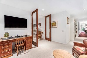 A room with a desk, chair, TV, open door, and a view into another room.
